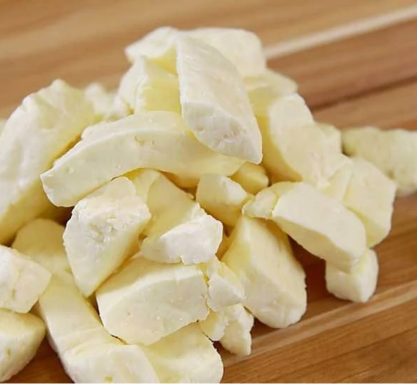 A pile of fresh, creamy white cheese curds resting on a wooden cutting board.