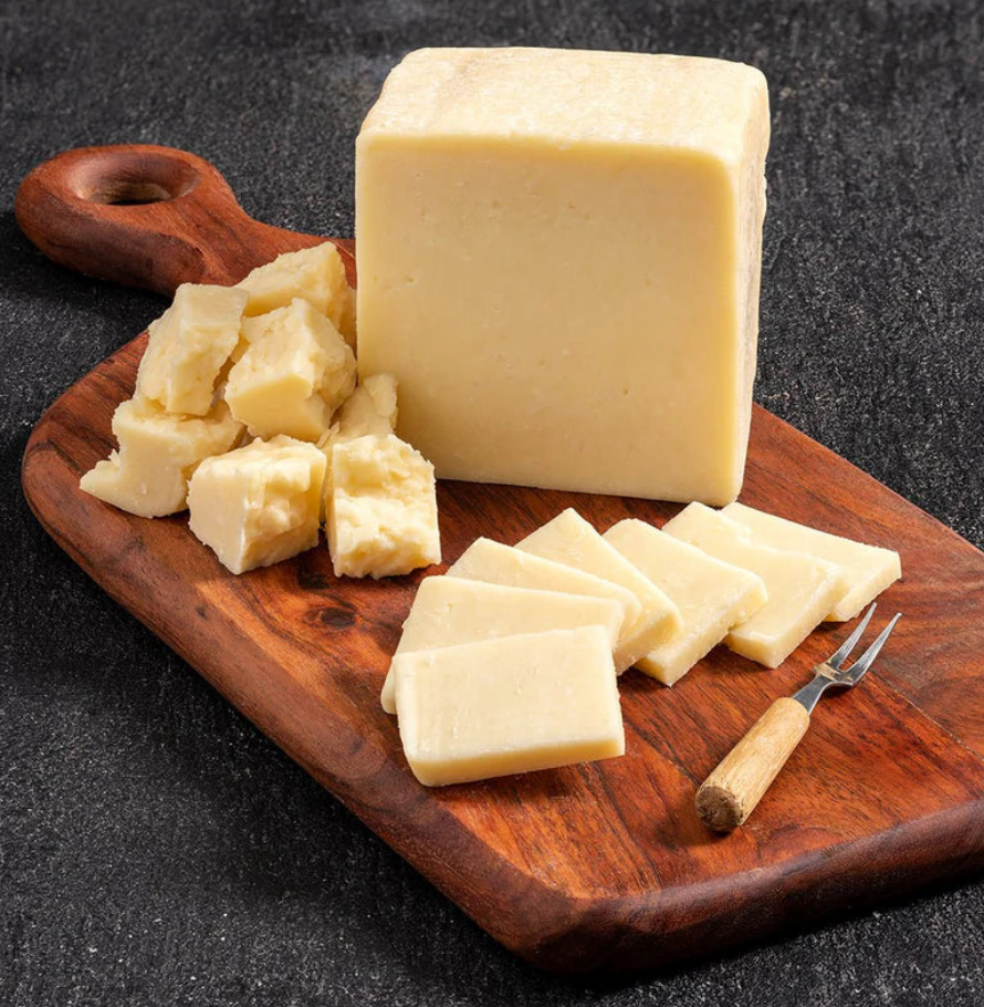 A block of aged cheddar with cubes and slices on a rustic wooden serving board with a small cheese fork.