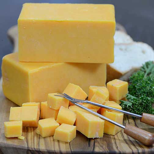 Blocks and cubes of orange Balderson cheddar cheese served with a fondue fork on a wooden board with bread and parsley.