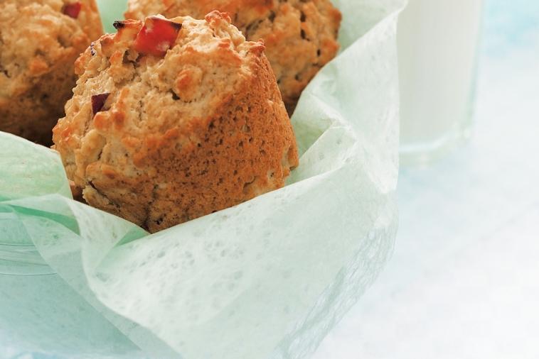 Golden brown apple oatmeal muffins with visible fruit chunks served in a bowl lined with light green parchment paper.