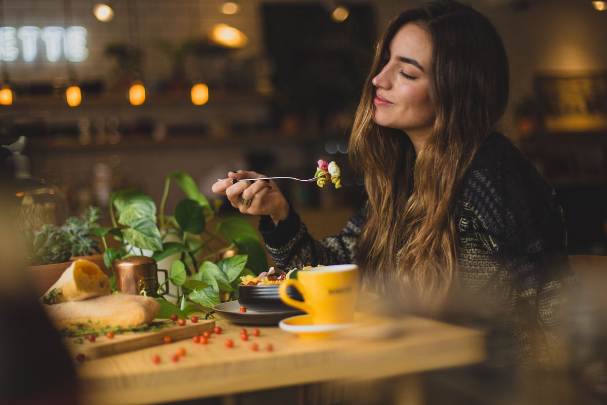 Woman with long brown hair enjoying a healthy meal at a wooden cafe table with a bright yellow mug.