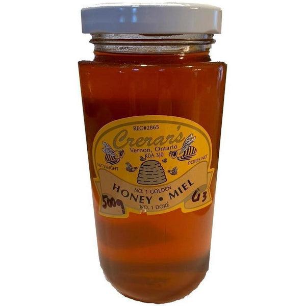 Crerar's Pure Golden Honey in a clear glass jar with a white lid and yellow label featuring bees and a beehive.